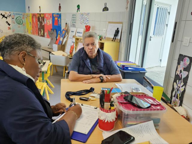 Two adults sit at a table in a bright art room, with colorful student artworks on the walls.
