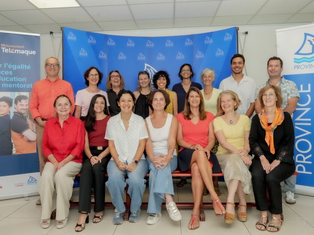 Group of adults smiling for a photo in front of blue event banners and a Province Sud backdrop, indoors on a red bench formation behind them.